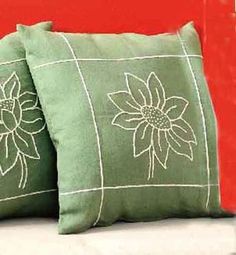 two green pillows sitting on top of a white couch next to a red pillow case