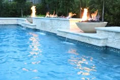 a fire pit in the middle of a pool with blue water and trees behind it