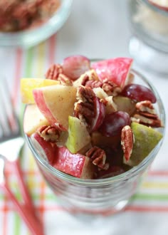 a glass filled with fruit and nuts on top of a white table cloth next to a fork