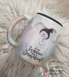 a white mug with a snowman painted on it sitting on top of a furry surface