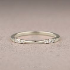 a white gold wedding band with five diamonds on it's side, in front of a gray background