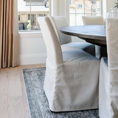 a dining room table with white chairs and a rug on the floor in front of it