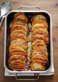 a pan filled with potatoes sitting on top of a wooden table next to a knife and fork