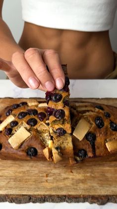 a person cutting up a banana bread with blueberries on it