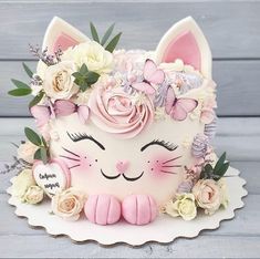 a white cake decorated with pink flowers and a cat's face on top of it