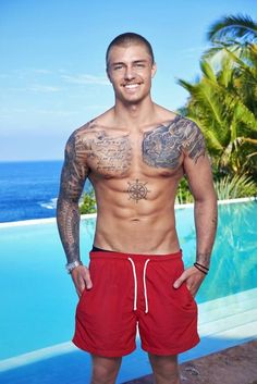 a man standing in front of a swimming pool with tattoos on his chest and arms