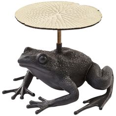 a black frog sitting under a table with a white umbrella on it's head