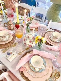 the table is set with pink and white dishes, plates, cups, and candles