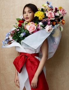 a woman in a red and white dress holding a bouquet of flowers on her shoulder