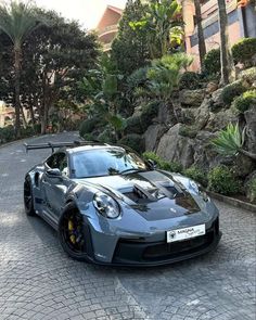 a grey sports car parked on the side of a road next to trees and bushes