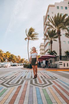 a woman is walking down the sidewalk in front of some buildings and palm trees on a sunny day