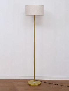 a floor lamp with a white shade on the base and a light bulb plugged in