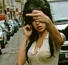 a woman covering her eyes while standing in front of parked cars on a city street