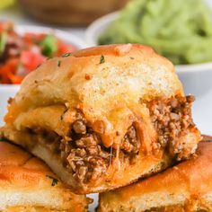 two sloppy joe sandwiches stacked on top of each other next to a bowl of guacamole