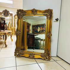 an ornate gold framed mirror sitting on the floor in front of a white door and table