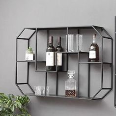 a metal shelf with bottles and glasses on it next to a potted plant in front of a gray wall