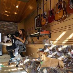 a woman sitting on a couch next to a dog in a living room with guitars hanging from the wall