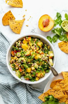 a white bowl filled with corn salsa next to tortilla chips and lime wedges