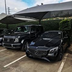 three cars parked in a parking lot under an awning with bushes and shrubs behind them