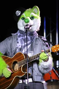 a person in a costume playing a guitar and singing into a microphone with an animal mask on