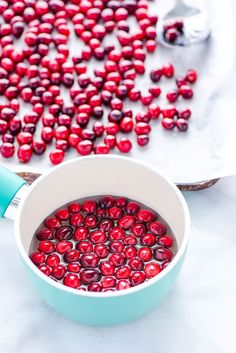 a pot filled with red berries next to a spoon and bowl full of cherries