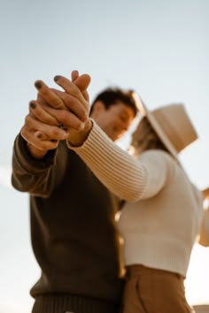 a man and woman holding hands while standing next to each other in front of the sky