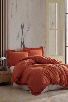 a bed with an orange comforter and pillows in a room next to a window