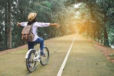 a woman riding a bike on the road with her arms spread out to the side