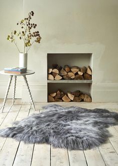 a living room with wood stacked on the floor and a fur rug in front of it