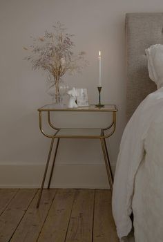 a small table with a candle on it next to a white bed and a nightstand