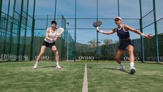 two women are playing tennis on an outdoor court with green grass and fence surrounding them