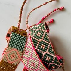 two handmade bracelets hanging from twine on a white counter top with pink and green beads