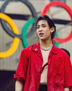 a young man wearing a red shirt stands in front of the olympic rings