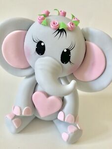 an elephant figurine with pink flowers on its head and tusks, sitting in front of a white background