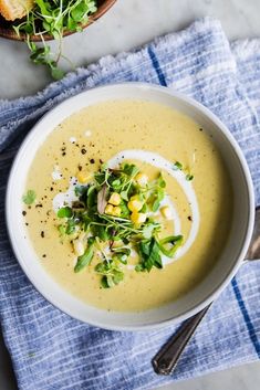 a white bowl filled with soup and topped with green garnish next to a plate of bread