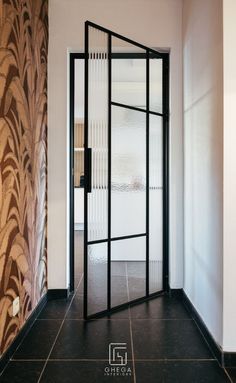 an open glass door in the middle of a room with black tile flooring and wallpaper