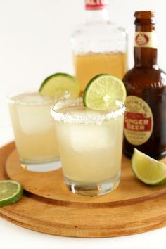 two margaritas on a wooden platter with bottles of alcohol in the background