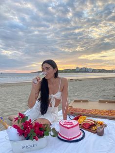 a woman sitting at a table with a cake and wine in front of her on the beach