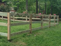 the fence is made of wood and has pink flowers growing on top of it, along with green grass