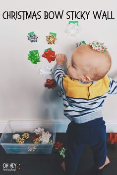 a baby standing next to a wall with christmas bows on it