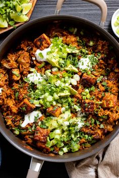 a skillet filled with meat and vegetables on top of a wooden table next to other dishes