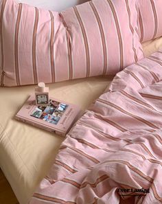 a bed with pink and white striped comforter next to a book on top of it