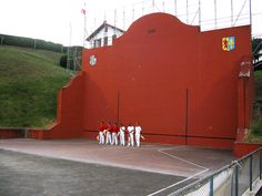 a group of people standing on top of a tennis court next to a red wall