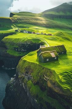 an aerial view of some green hills with houses on the top and water below them