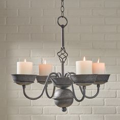 a chandelier with five lit candles in front of a brick wall and floor