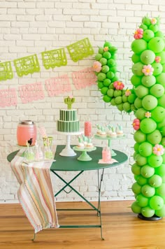 a table topped with green balloons next to a cake and cupcakes on top of plates