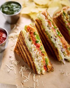 two sandwiches cut in half sitting on top of a table next to chips and dipping sauce