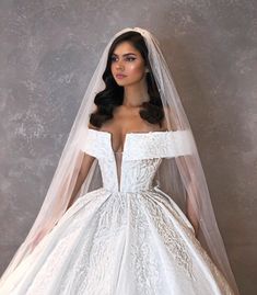 a woman in a white wedding dress with a veil on her head and an off the shoulder gown