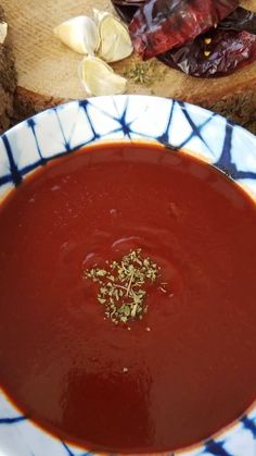 a bowl of tomato soup with herbs on the table next to sliced garlic and bread