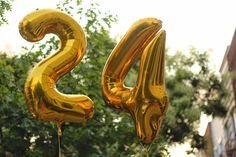 two gold balloons shaped like the numbers twenty and thirty hanging in front of some trees